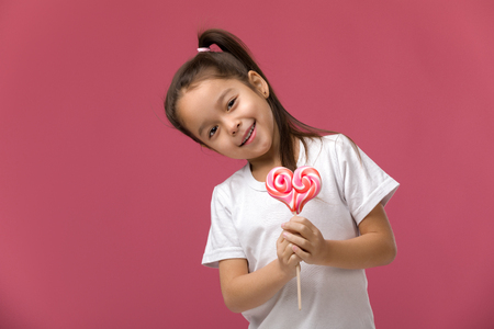 Beautiful cute little child girl with sweet candy lollipop isolated on pink backgroundの写真素材