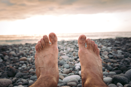 Legs of man on the beach at sunset in seaの写真素材