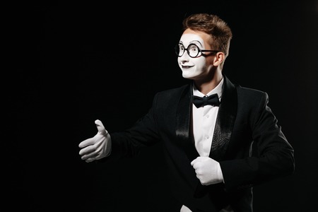 portrait of mime man in tuxedo and glasses giving hand for handshake on black backgroundの写真素材