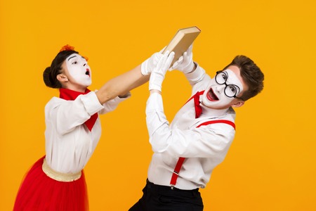 portrait of mime couple artist quarreling and reading book isolated on yellow backgroundの写真素材