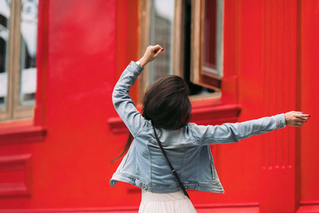 attractive woman in sunglasses and dress dancing on the city streets on a sunny day. girl against a red wallの写真素材