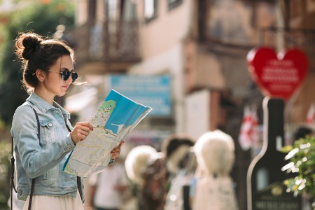 beautiful caucasian tourist woman looking at the map on the street of city