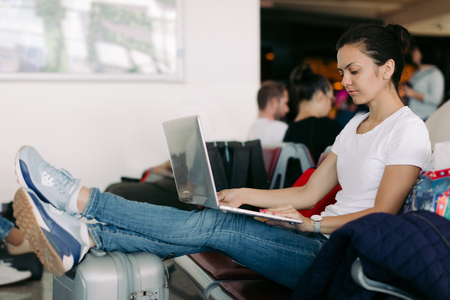 Young female passenger using laptop computer at airport while waiting for her flightの写真素材