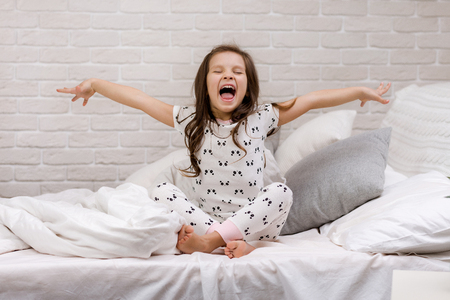 cute happy little child girl in pyjamas in bed. good morningの写真素材