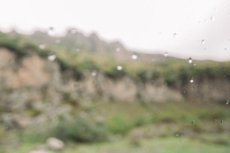 blurred background of drops of rain on the glass against the mountains