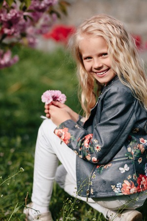 portrait of a beautiful little child girl with sakura flowers on a sunny spring dayの写真素材