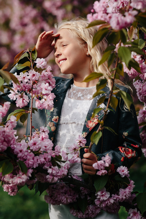 portrait of a beautiful little child girl with sakura flowers on a sunny spring dayの写真素材