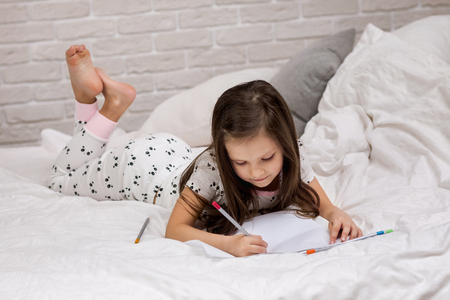 cute little girl drawing pictures while lying on bed. Kid painting at homeの写真素材