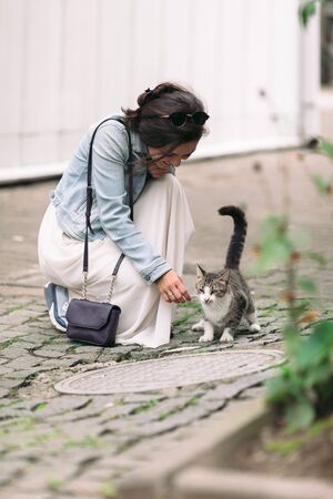 attractive woman in dress plays with cat in old courtyardの写真素材