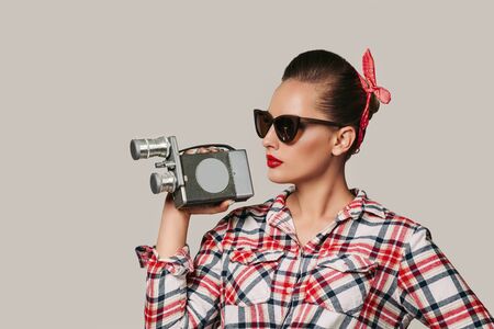 pin-up girl in plaid shirt and sunglasses holding old vintage camera. copy space for text
