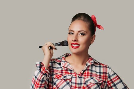 smiling pin-up girl in plaid shirt holding make-up brush. retro style woman applying blusher. copy space for textの写真素材