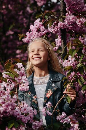 portrait of a beautiful little child girl with sakura flowers on a sunny spring day