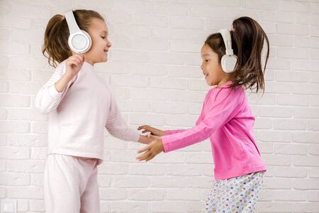 little children girls listening to the music with the headphones and dancing on bed. pajama party and friendship.の写真素材