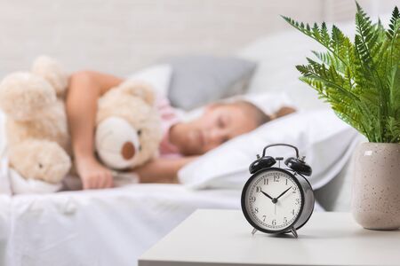 Cute little child girl sleeping with teddy bear in her bed. focus on clockの写真素材