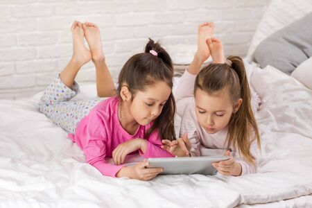 two cute children girls use digital tablet in bed. child playing on tablet pc.の写真素材