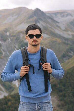 Young tourist man with a backpack against the background of the Caucasus Mountains, Georgia on a foggy dayの写真素材