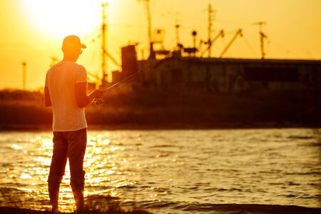 Young man fishing at sea from the shore at sunset. soft lightの写真素材