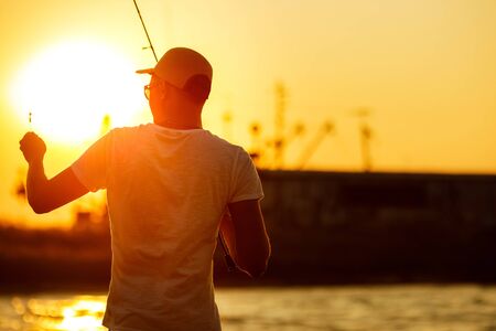 Young man fishing at sea from the shore at sunset. soft lightの写真素材