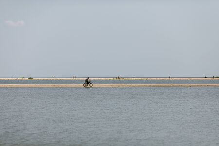Berdyansk, Ukraine - August 10, 2019: woman on a bicycle rides along the shore of the Sea of Azov in summer. Sea of Azovのeditorial素材