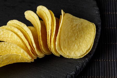 Salty delicious potato chips on wood background
