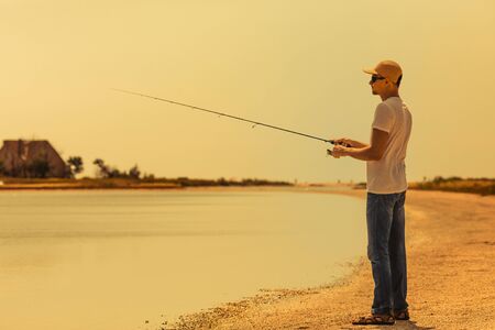 Young man fishing at sea from the shore. fisherman uses spinningの写真素材