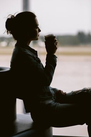 silhouette of woman waiting for flight aircraft. Airline passenger girl drinks coffeeの写真素材
