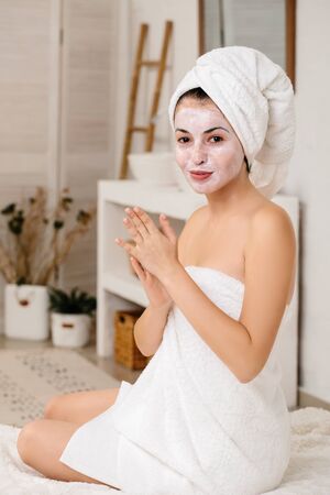 young woman with towel is applying mask on her face at home. Skin care.の写真素材