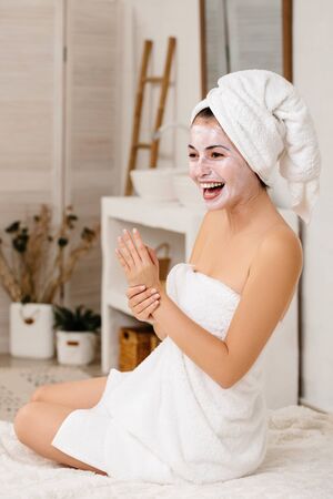 smiling woman with towel is applying mask on her face at home. Skin care.の写真素材