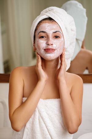 Woman with towel is applying mask on her face at home, close-up. Skin care.の写真素材