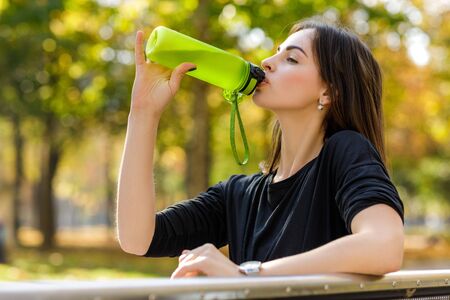 happy athletic woman with a bottle of water after running. young beautiful girl drinking water in parkの写真素材