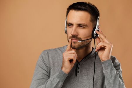 doubting call center worker man isolated on beige background. Young cute employee telesales agent using headset.の写真素材