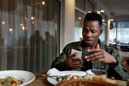 young disappointed surprised african american man messaging online, checking social networks in cafe. copy spaceの写真素材