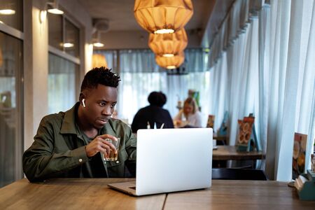 Cheerful young african american man in headphones using computer in cafeの写真素材
