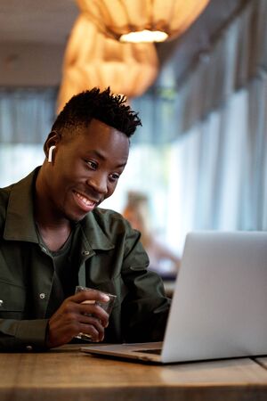 Cheerful young african american student man in headphones using computer in cafe. Online video chat with friendsの写真素材
