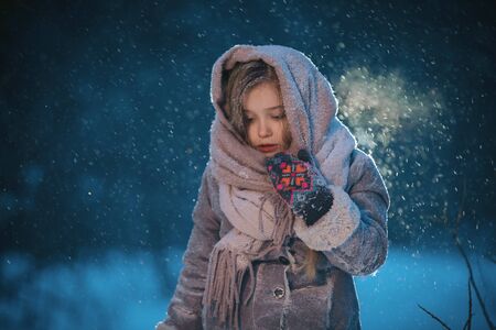 portrait of beautiful cute little child girl in shawl in the forest in winter eveninig. snowing and snowstormの写真素材