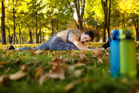 happy sporty woman stretching on green grass in park in sunny day