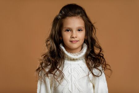 Cute smiling little child girl in white sweater looking to camera on beige background. Human...