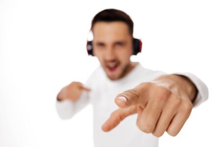 handsome smiling young man in headphones listening to music and points hand at you, isolated on white background. focus on handの写真素材