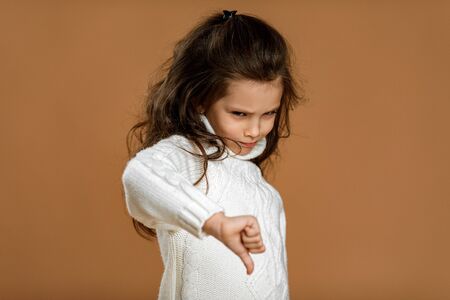 Cute little child girl in white sweater showing the thumbs down gesture on beige background.の写真素材