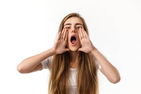 Portrait of young happy woman calling someone on white background. girl holding hands on mouth calling for someoneの写真素材