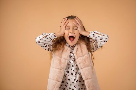 Cute little girl is closing her ears with her hand and screaming on beige background.の写真素材