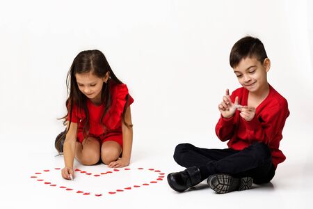 Happy romantic little couple girl and boy make a big heart shape out of small paper hearts on the floor isolated on white background. St. Valentines Dayの写真素材