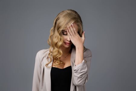 Portrait of beautiful sad woman with hand on face on gray background. young woman feeling stress and headacheの写真素材