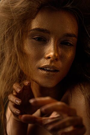 Fashion art portrait of female actress plays the role of a cat, lion or tiger. concept of wild animal inside every woman. beaty woman with gold metallic body and hair on dark background.の写真素材