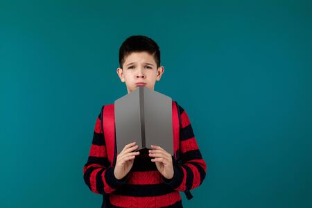 little cheerful school boy reading a book over blue background. child covers his face with book. blank space on book for your textの写真素材