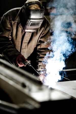 worker in protective uniform and mask welding metal. man using electric welding machineの写真素材