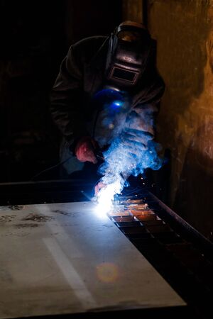 worker in protective uniform and mask welding metal. man using electric welding machine