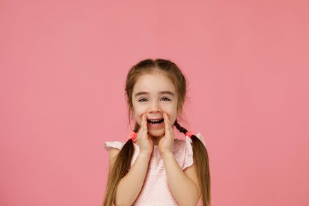 child calling someone. cute little girl shouting and holding her hand near her mouth on studio pink backgroundの写真素材