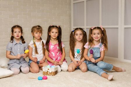 happy little child girls with basket with painted Easter eggs smiling while sitting on the floor of the room. friends celebrate Easter togetherの写真素材