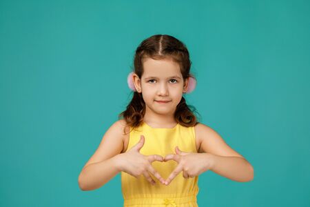 Cute smiling little child girl making heart-shape gesture on blue background.